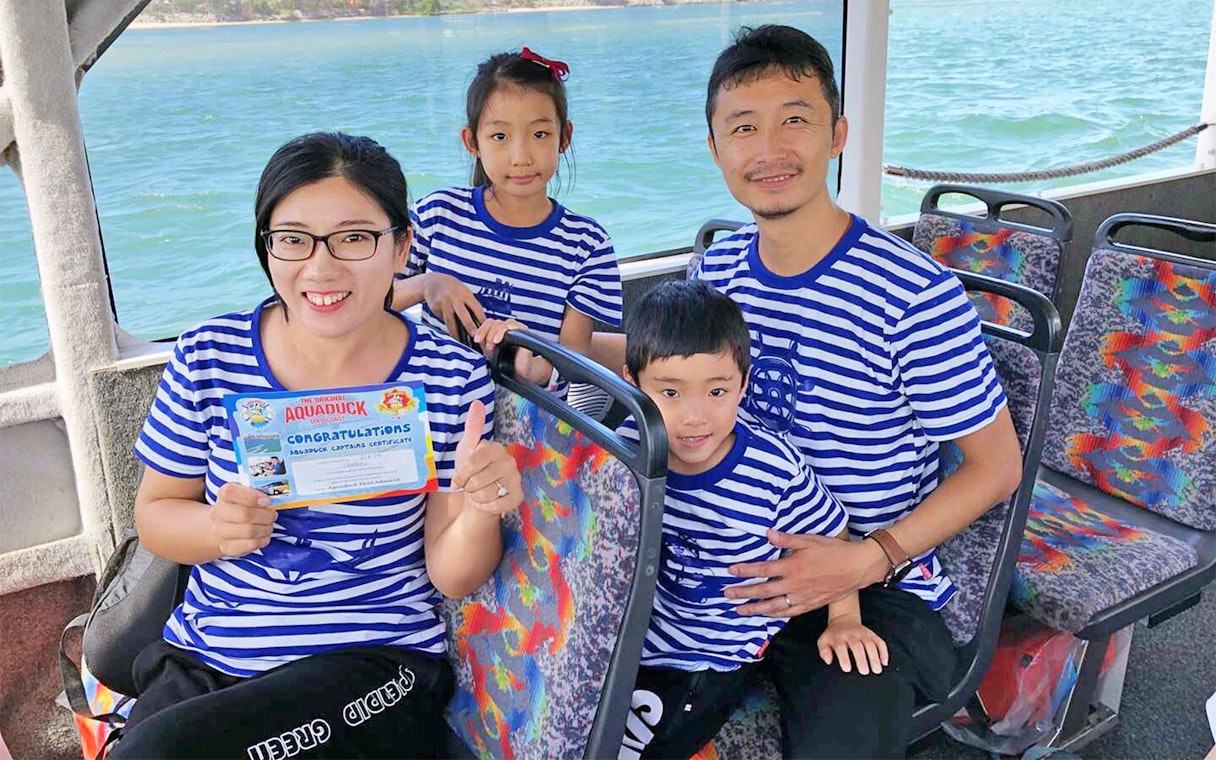 Family on Aquaduck tour holding certificate, Sunshine Coast water view.