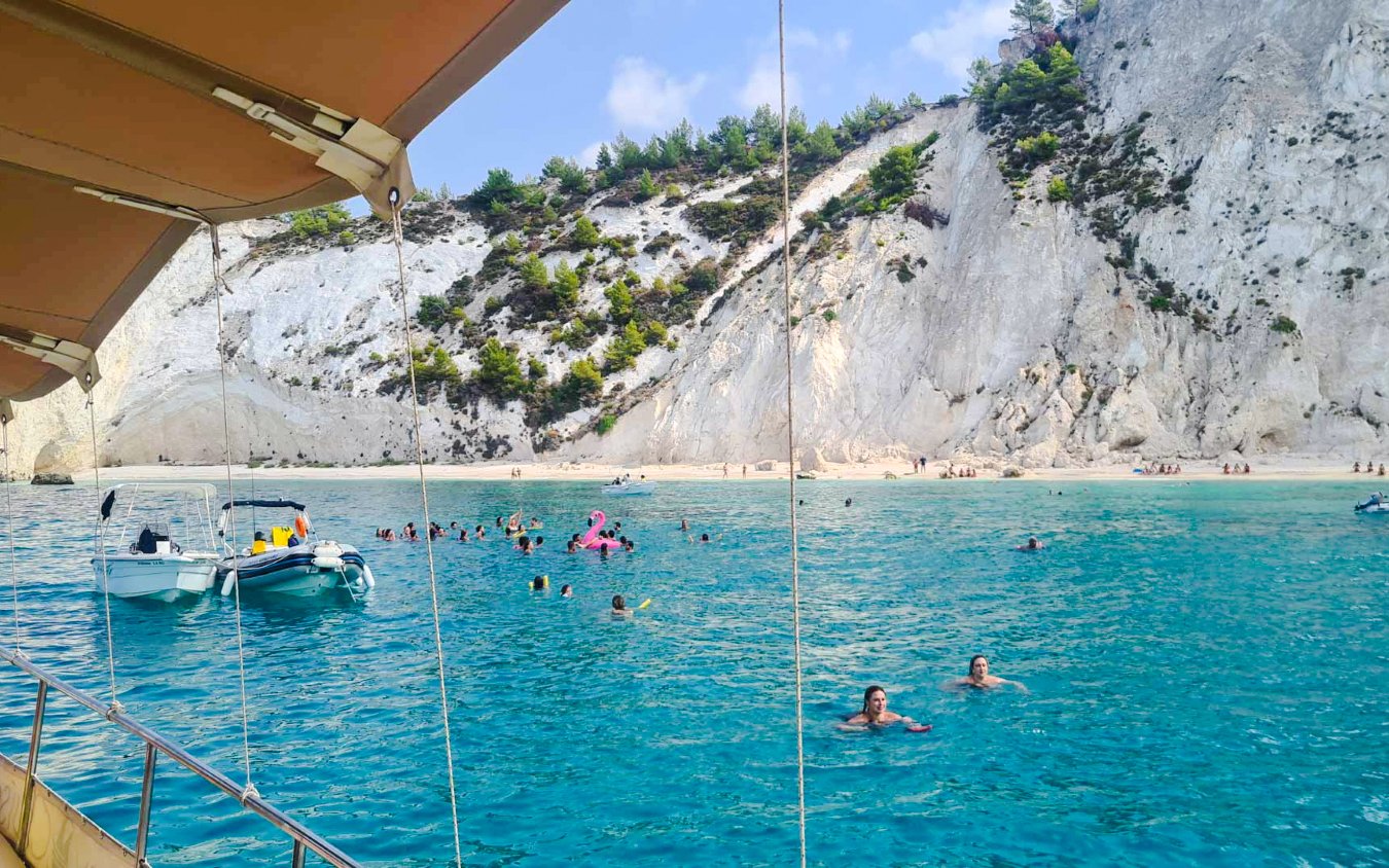 People swimming near a boat in turquoise waters with rocky cliffs in Kefalonia.