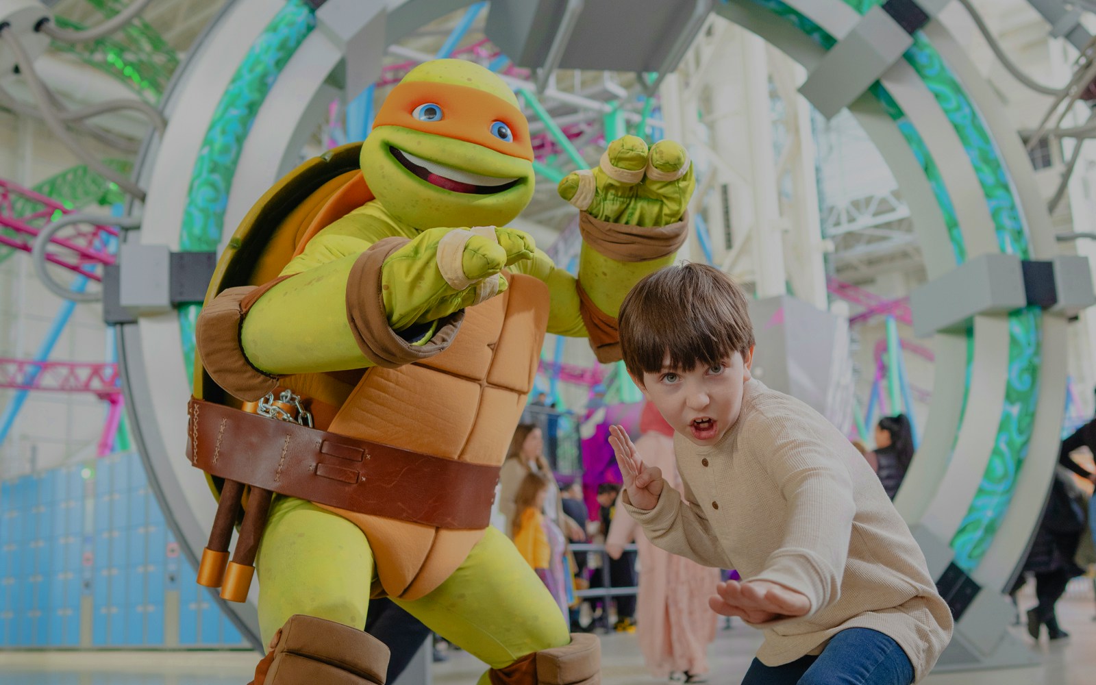 Child posing with Teenage Mutant Ninja Turtle character at an indoor amusement park.