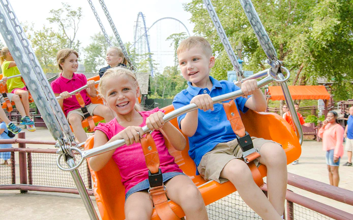 Children enjoying Charlie Brown's™ Wind-Up ride at Cedar Point with roller coaster in background.