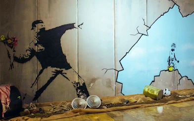 Street art mural at Banksy museum featuring a figure throwing flowers and a child with a bucket.