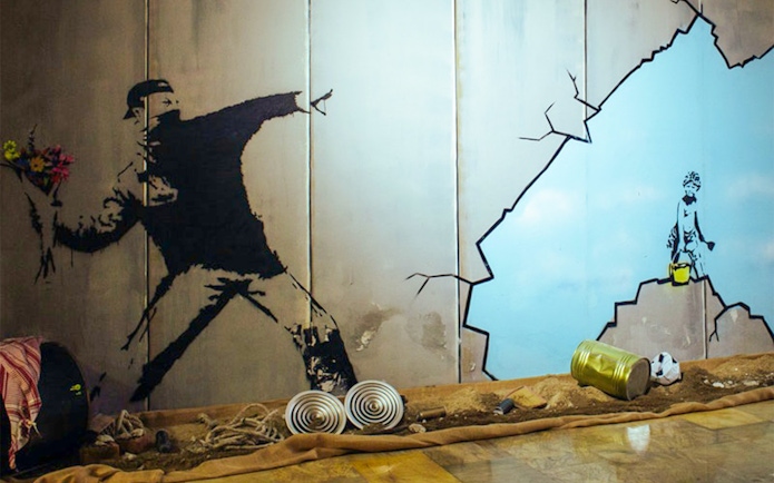 Street art mural at Banksy museum featuring a figure throwing flowers and a child with a bucket.