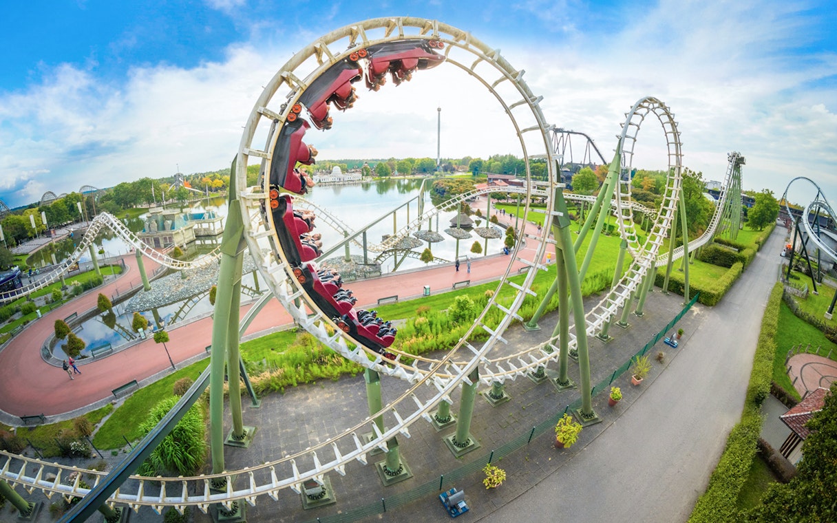 Roller coaster loop at Heide Park with riders and scenic park view.