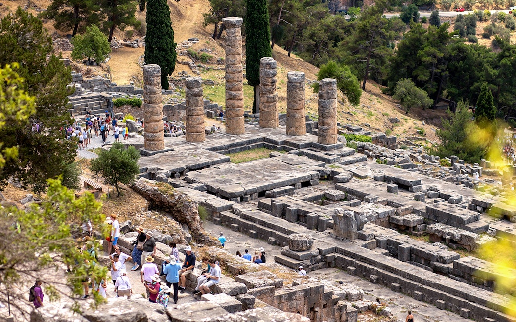 Visitors exploring ancient ruins at the Delphi archaeological site in Greece.