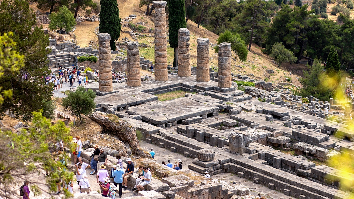 Visitors exploring ancient ruins at the Delphi archaeological site in Greece.
