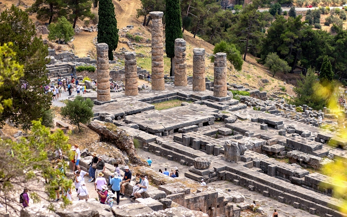 Visitors exploring ancient ruins at the Delphi archaeological site in Greece.
