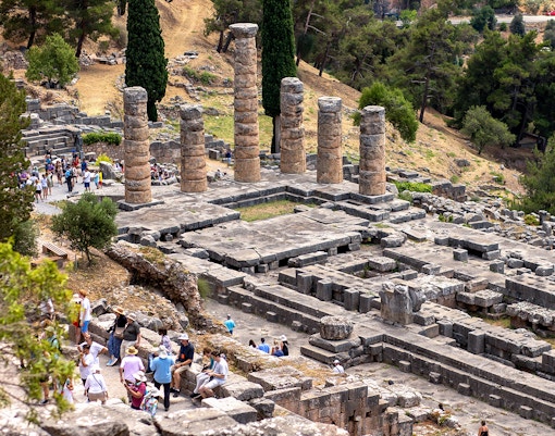Visitors exploring ancient ruins at the Delphi archaeological site in Greece.