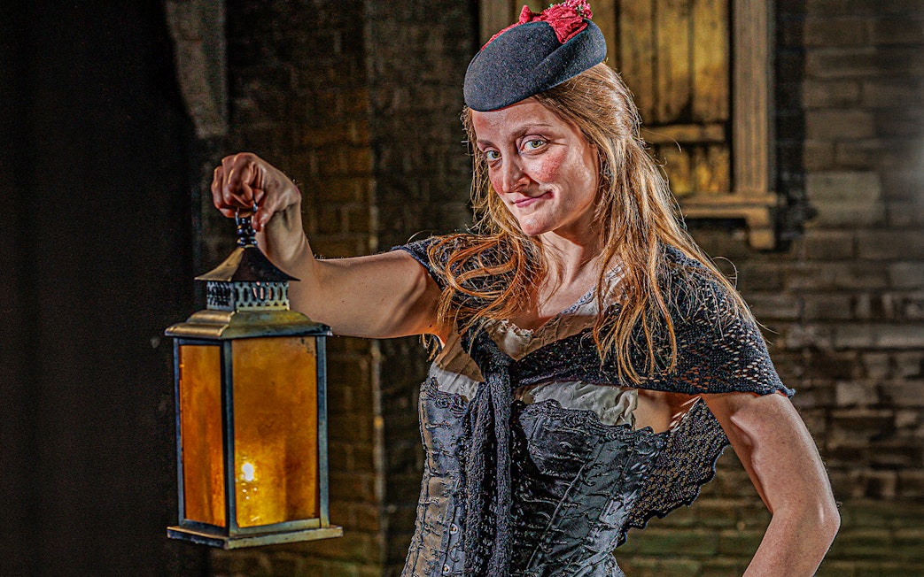Guide in period costume holding lantern at London Dungeon.