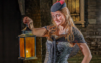 Guide in period costume holding lantern at London Dungeon.