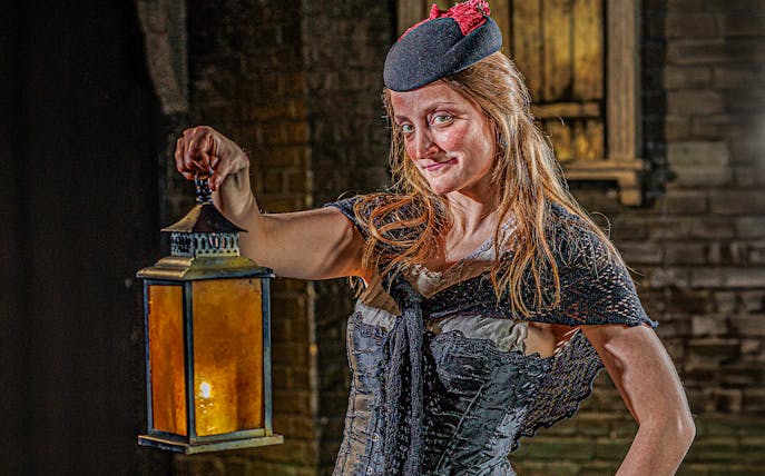 Guide in period costume holding lantern at London Dungeon.