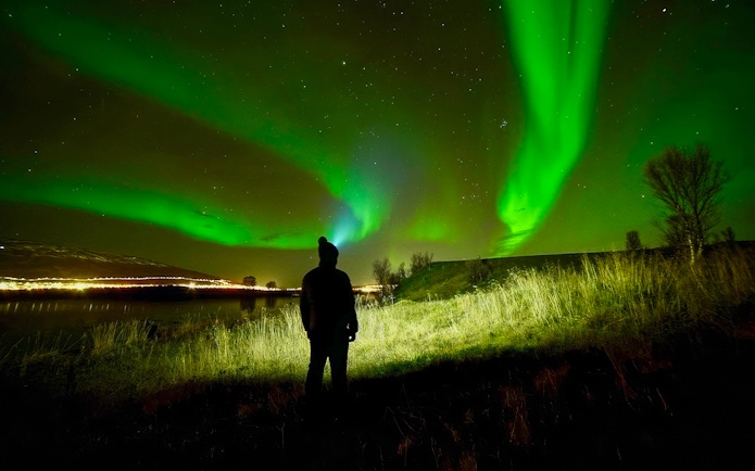 Person watching Northern Lights in night sky during aurora borealis tour.