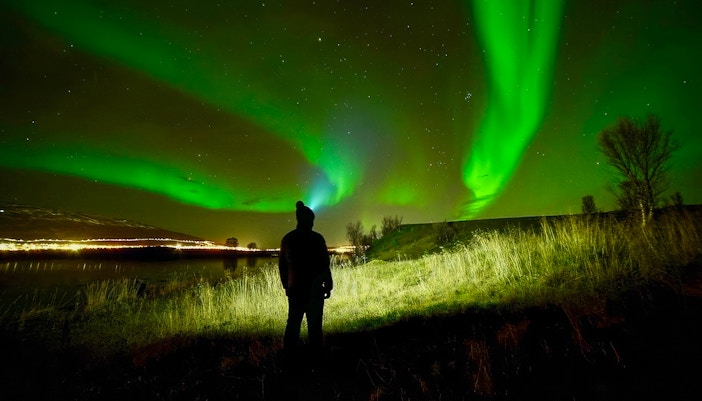 Person watching Northern Lights in night sky during aurora borealis tour.
