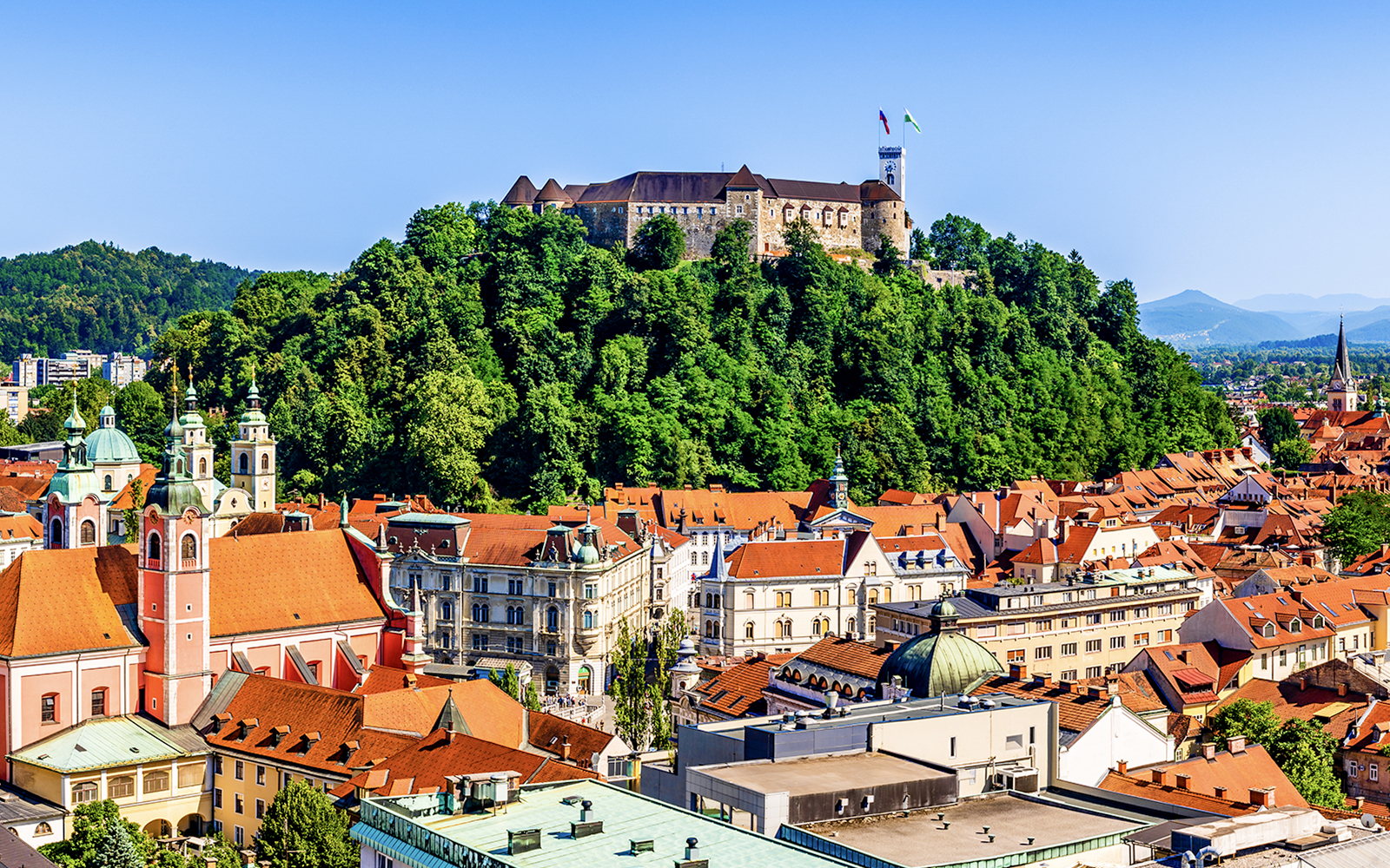 Ljubljana Castle atop a forested hill overlooking the city rooftops.