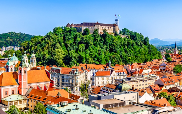 Ljubljana Castle atop a forested hill overlooking the city rooftops.