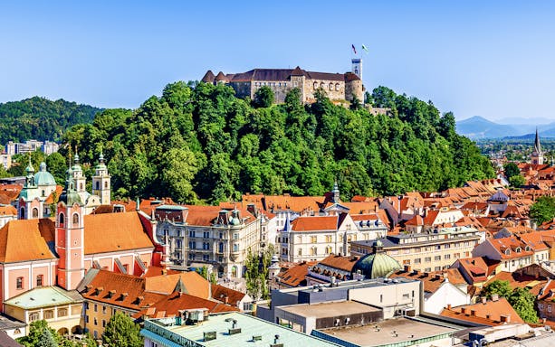 Ljubljana Castle atop a forested hill overlooking the city rooftops.