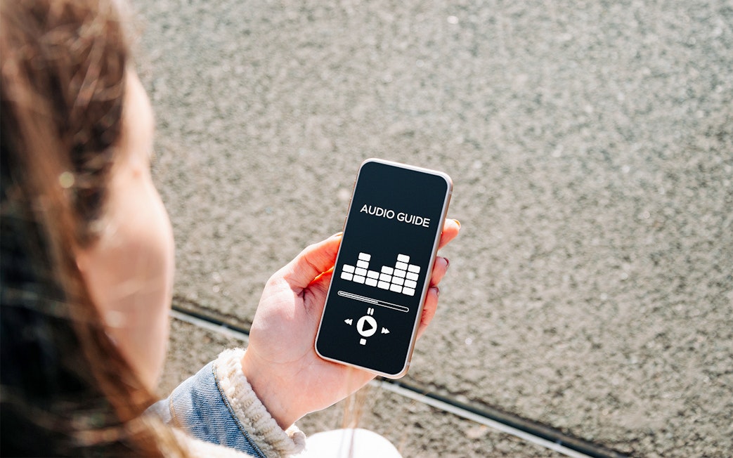 Person holding smartphone with audio guide app on screen.