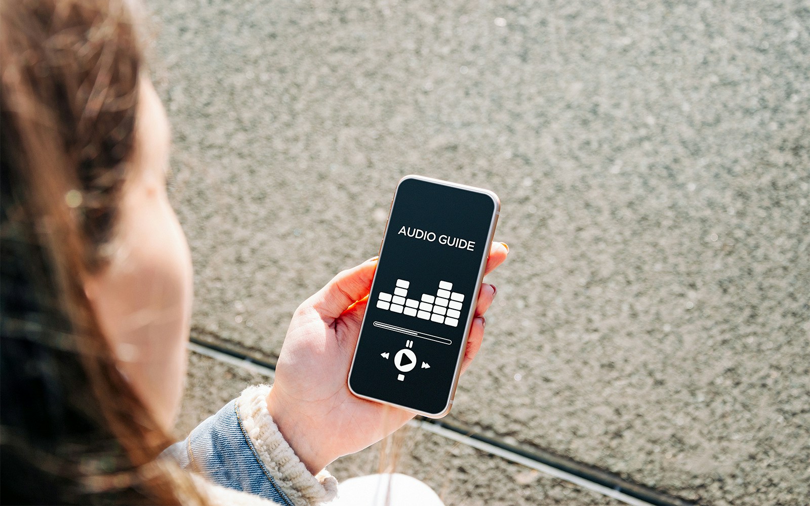 Person holding smartphone with audio guide app on screen.