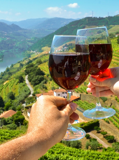 Wine glasses toasting over vineyards in Douro Valley, Portugal.