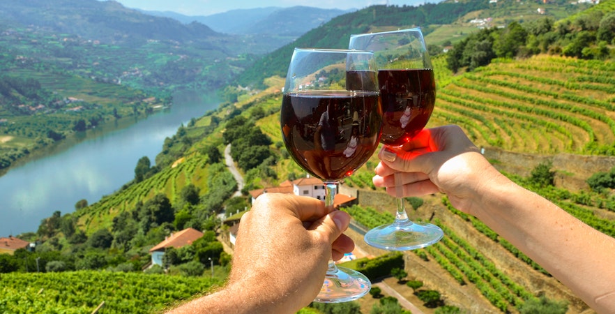 Wine glasses toasting over vineyards in Douro Valley, Portugal.