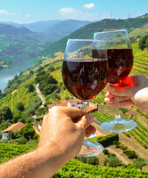 Wine glasses toasting over vineyards in Douro Valley, Portugal.