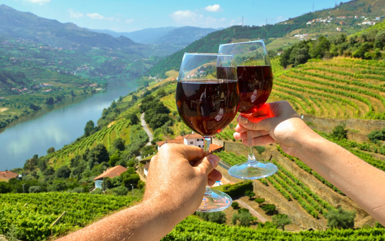 Wine glasses toasting over vineyards in Douro Valley, Portugal.