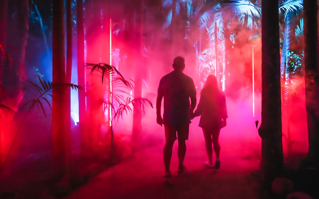 Tourists walking through red-lit forest at Astra Lumina, Currumbin Wildlife Sanctuary.