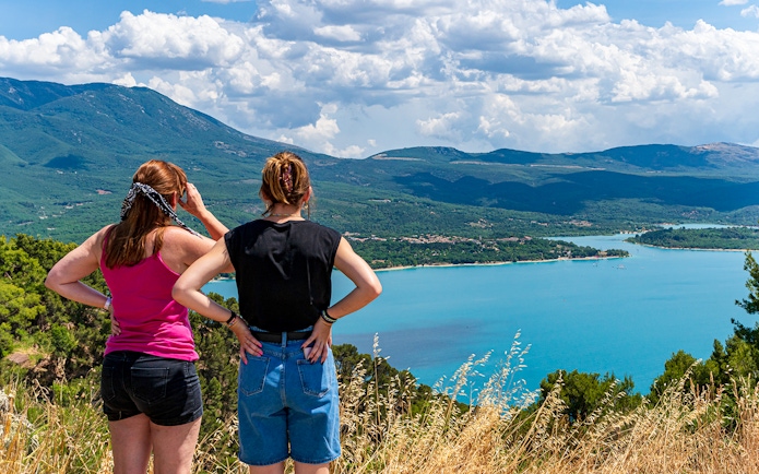 Two people overlooking the Lake of St Croix in France with clear blue waters and surrounding mountains.