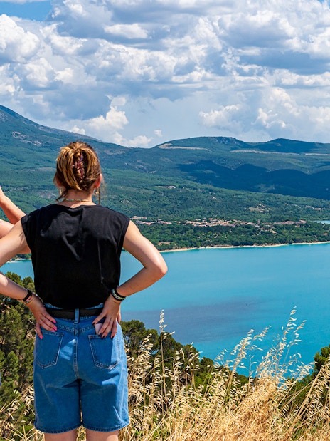 Two people overlooking the Lake of St Croix in France with clear blue waters and surrounding mountains.