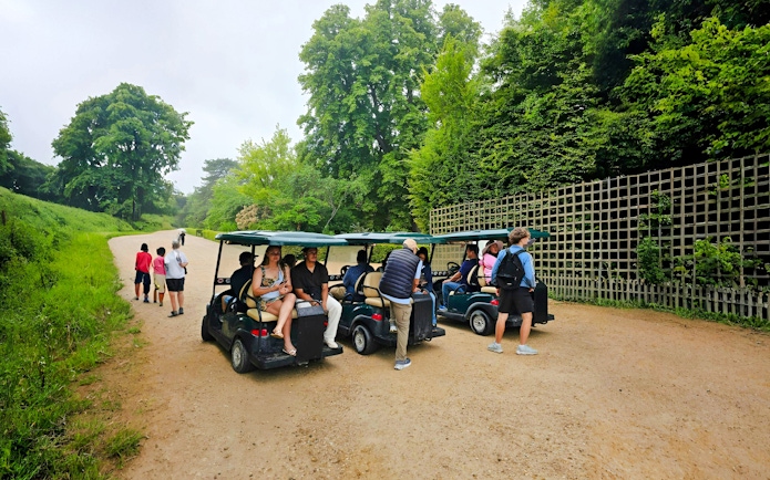 Tourists on golf carts during Versailles guided tour through lush gardens.