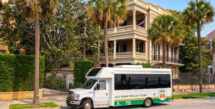 Old Town Trolley in front of historic Charleston mansion with palm trees.