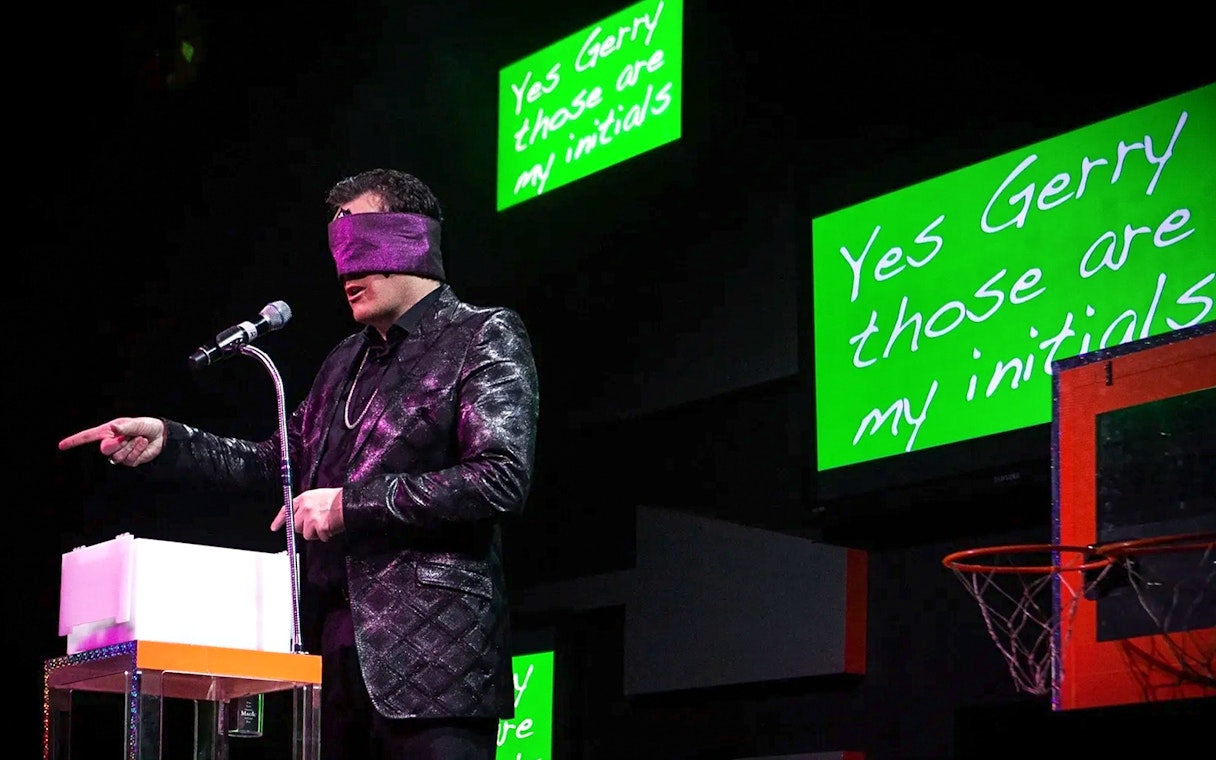 Performer blindfolded on stage during The Mentalist show, pointing at audience.