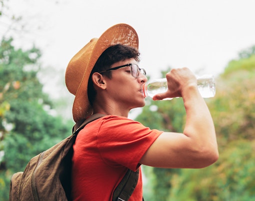 Traveler drinking water from a bottle in a lush outdoor setting.