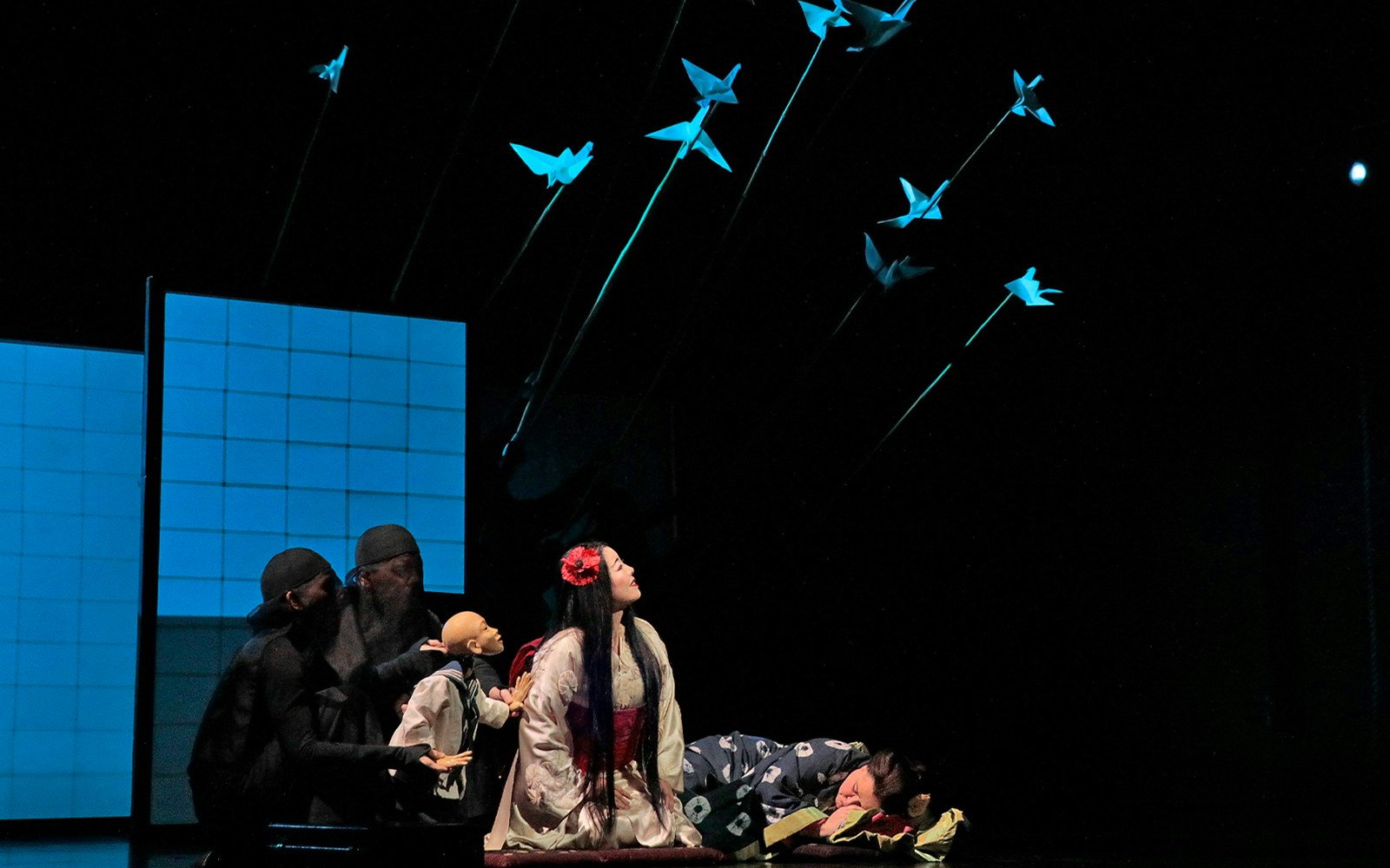 Opera performers in Madama Butterfly scene with puppets and origami birds.