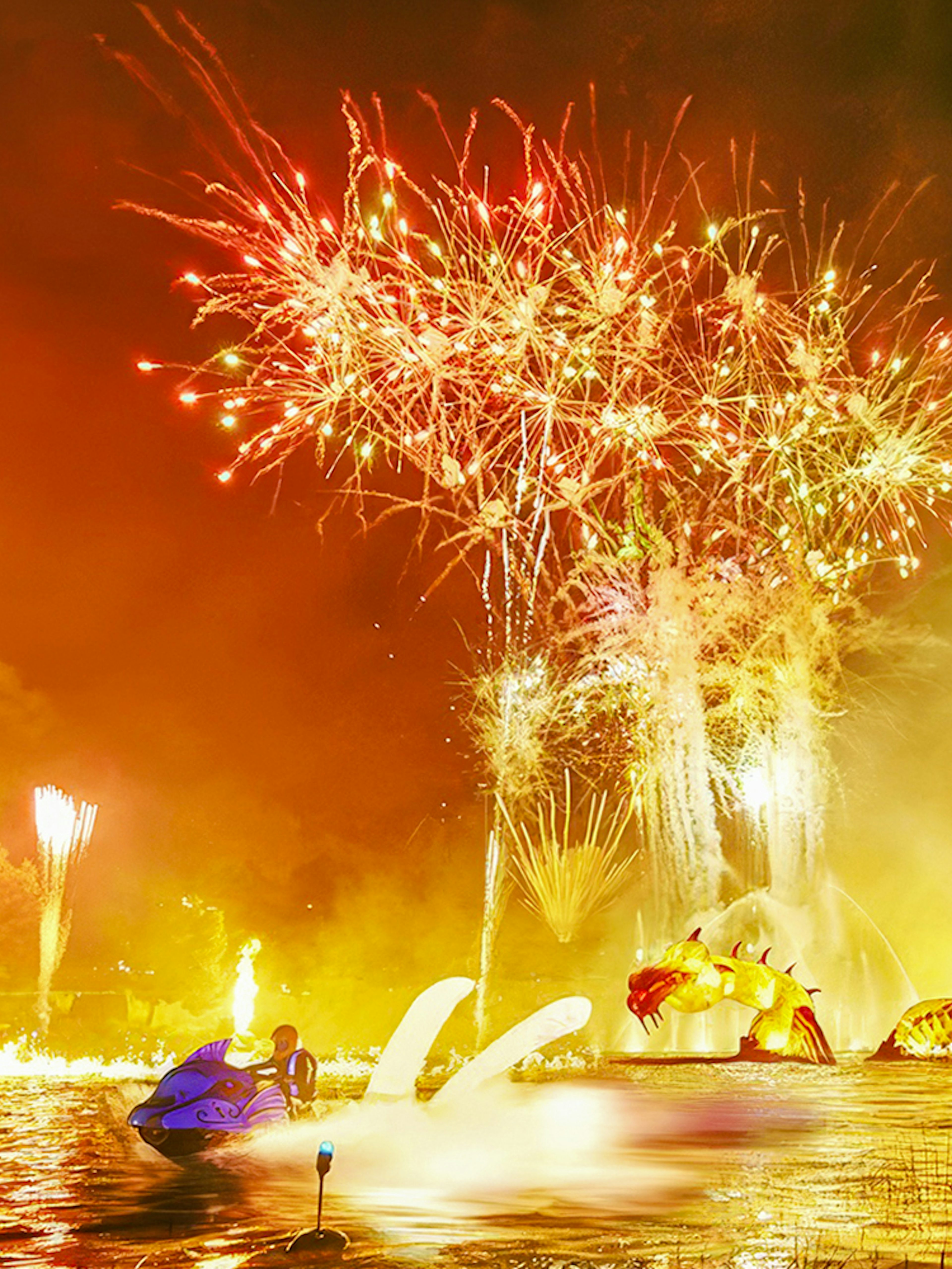 Fireworks display over water with dragon sculpture at PortAventura Park.