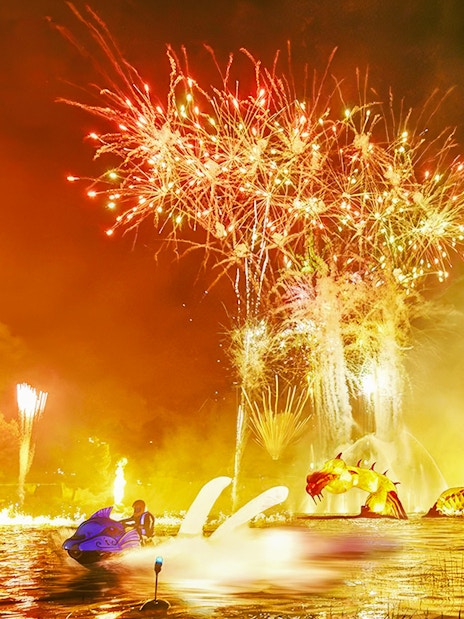 Fireworks display over water with dragon sculpture at PortAventura Park.