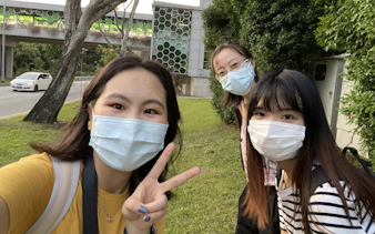 Three people wearing masks outdoors in Singapore, near a modern building, during a city exploration game.