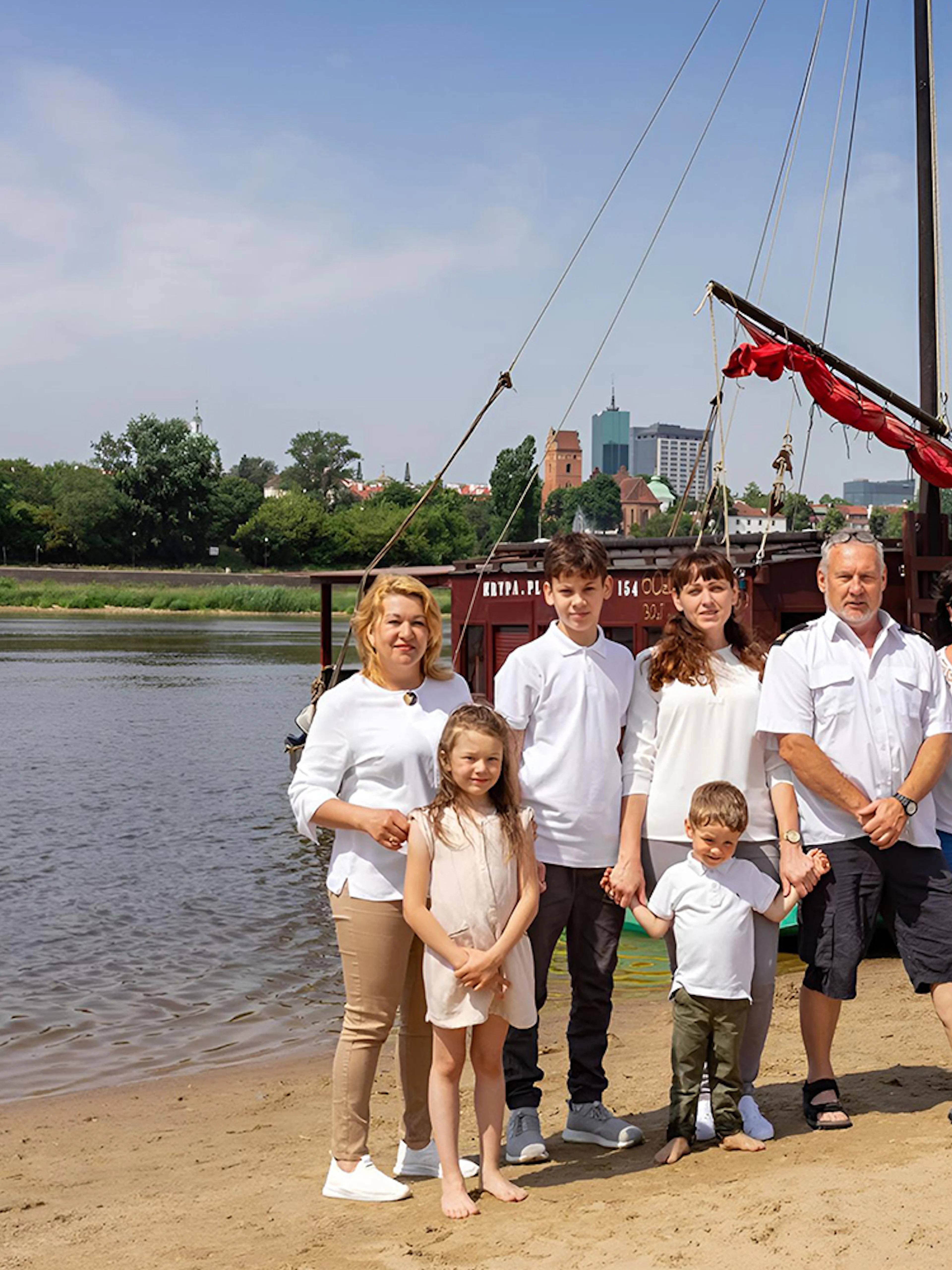 Family posing on the Vistula Riverbank with a traditional Galar boat in the background.