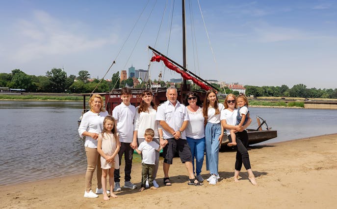 Family posing on the Vistula Riverbank with a traditional Galar boat in the background.