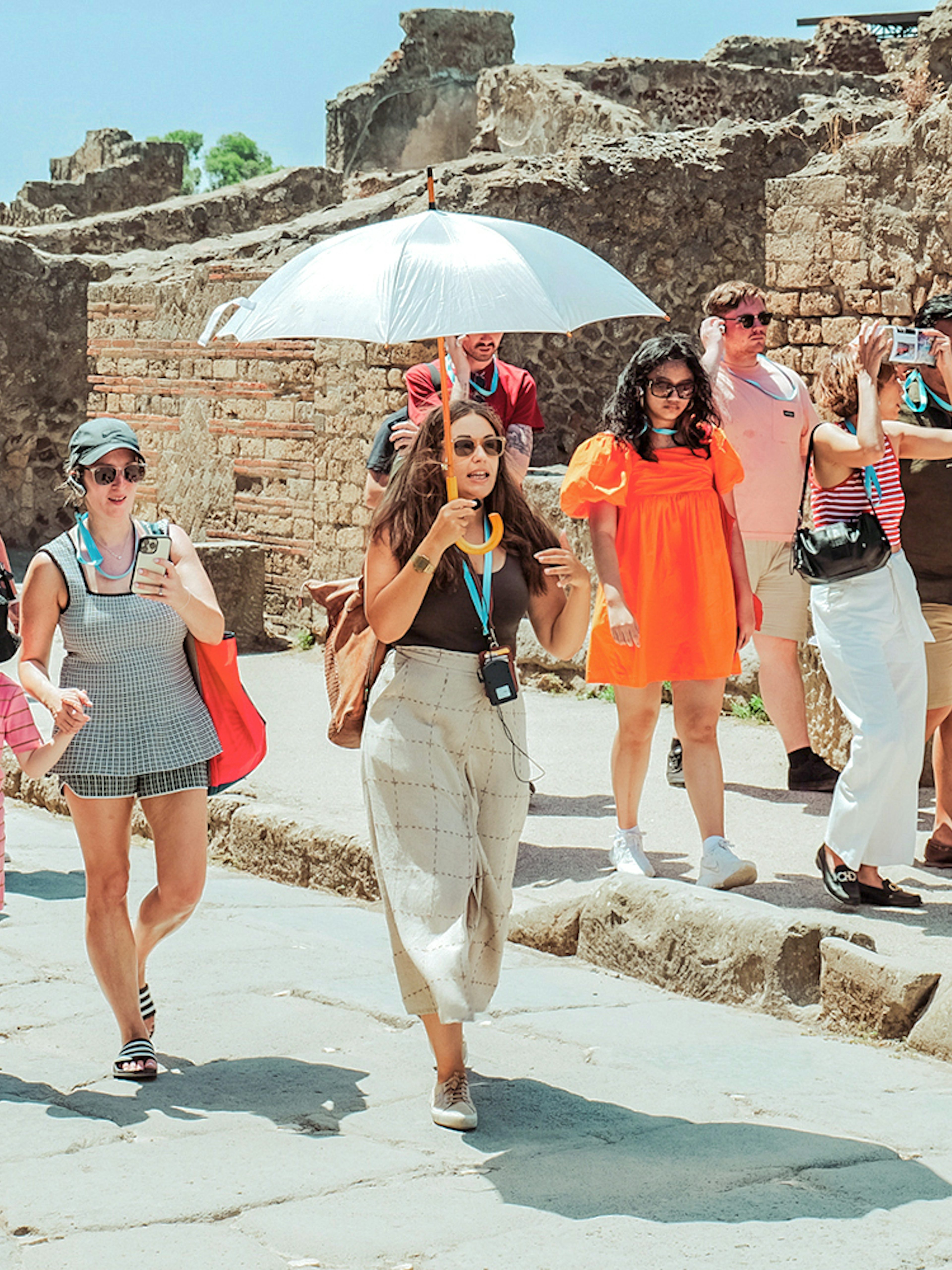 Guide with umbrella leading a tour group through ancient ruins in Pompeii.