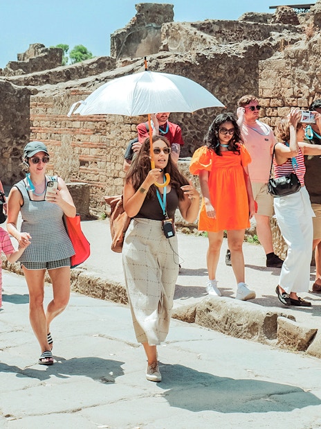 Guide with umbrella leading a tour group through ancient ruins in Pompeii.
