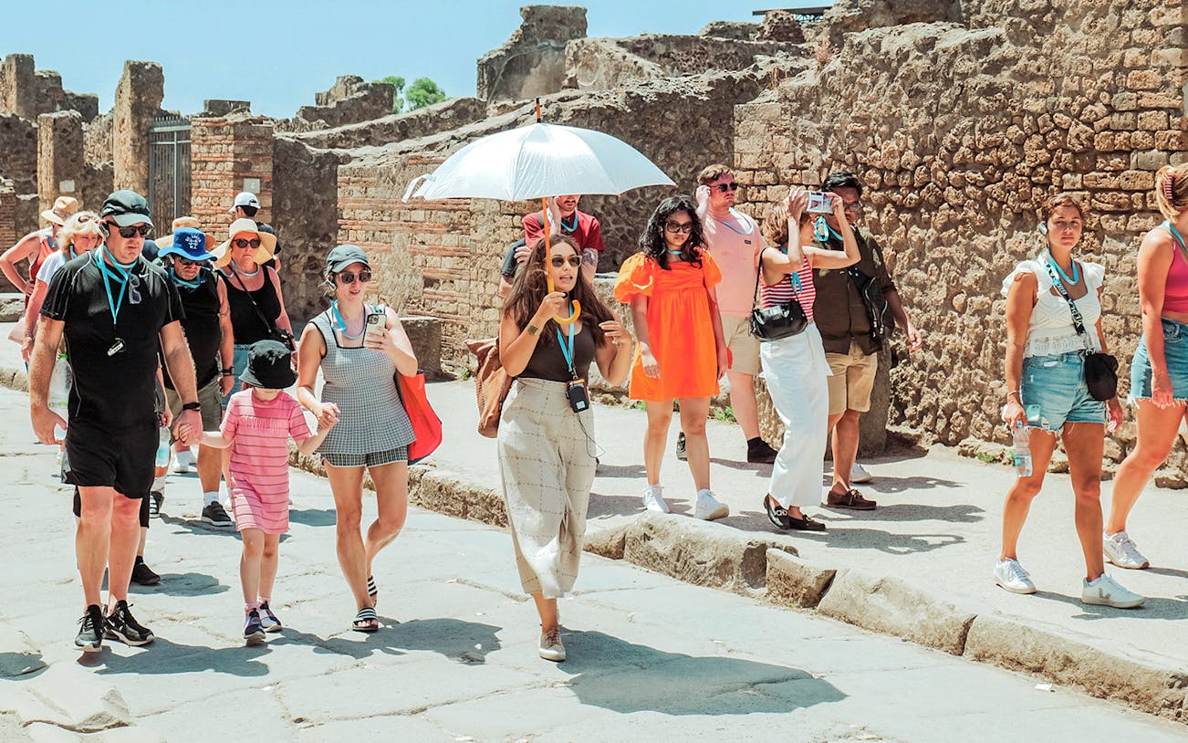 Guide with umbrella leading a tour group through ancient ruins in Pompeii.