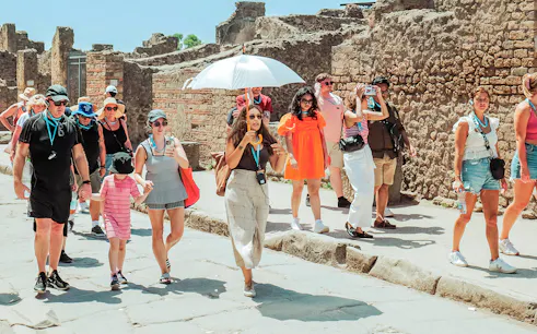Guide with umbrella leading a tour group through ancient ruins in Pompeii.