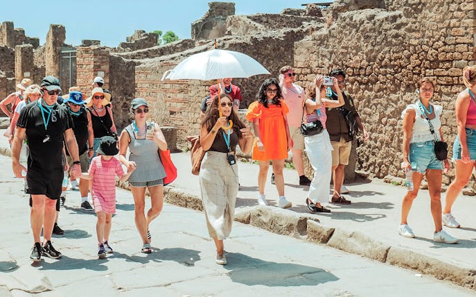 Guide with umbrella leading a tour group through ancient ruins in Pompeii.