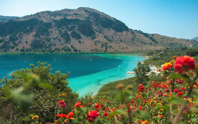 Lake Kournas with vibrant flowers and mountainous backdrop, Crete.