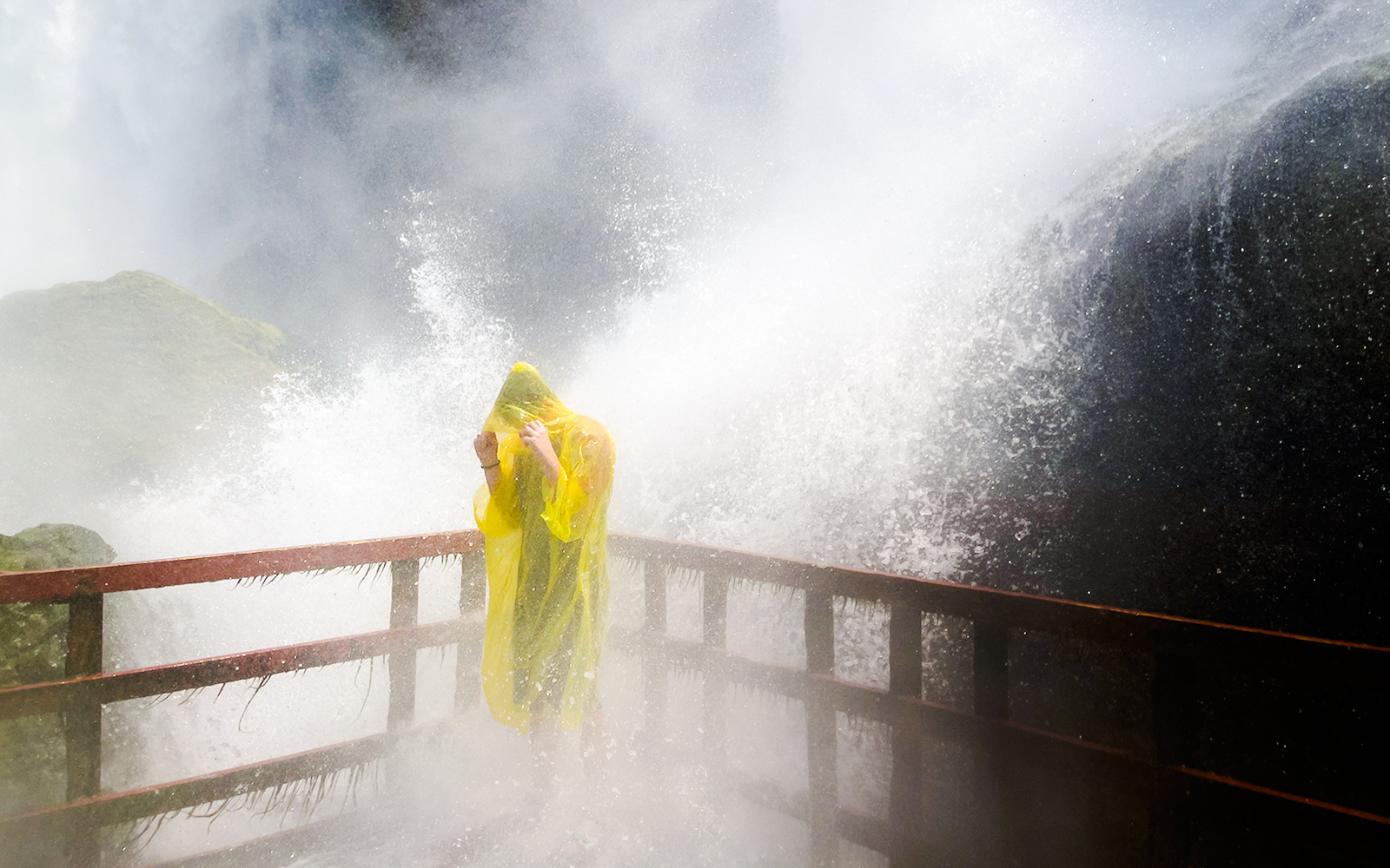 Person in yellow poncho on Cave of the Winds walkway with waterfall spray.