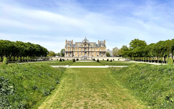 Château de Maisons with manicured gardens and tree-lined path in Maisons-Laffitte, France.