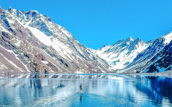 Person paddleboarding on Laguna del Inca with snow-capped Andes mountains, Portillo, Chile.
