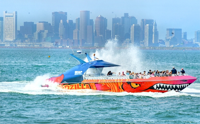 Thrill-seekers on CODZILLA boat ride in Boston Harbor with city skyline in background.