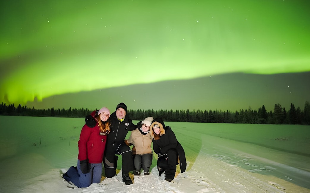 Guests on Northern Lights Discovery Tour under vibrant aurora borealis in snowy landscape.