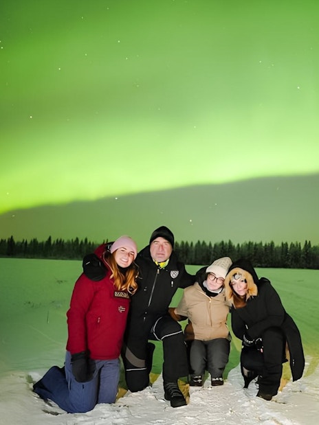 Guests on Northern Lights Discovery Tour under vibrant aurora borealis in snowy landscape.